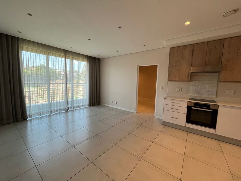 Modern open-plan living area featuring tiled floors, recessed lighting, and a sleek kitchen with built-in appliances and subway tile backsplash.