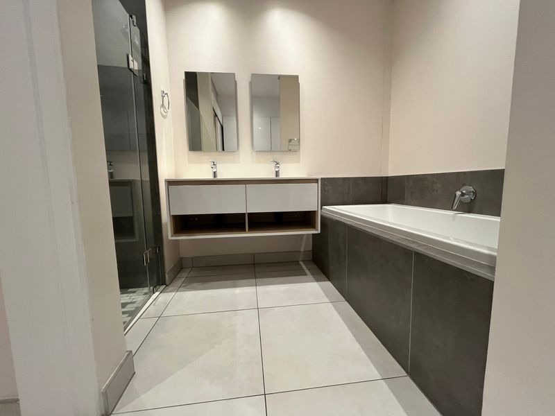 Modern bathroom featuring a double vanity, built-in bathtub, glass-enclosed shower, and contemporary large-format floor tiles with neutral wall finishes.