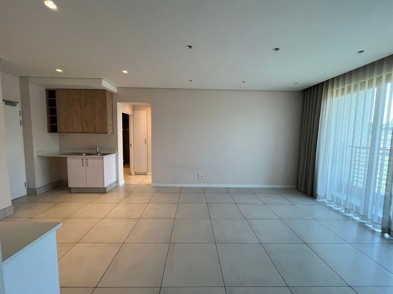 Spacious open-plan living area featuring large format floor tiles, recessed lighting, and a compact kitchenette with built-in cabinetry and sink.