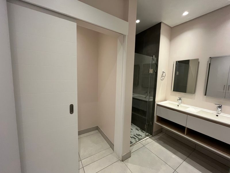 Modern bathroom featuring a double vanity with integrated sinks, a glass-enclosed shower, and a space-saving sliding door.