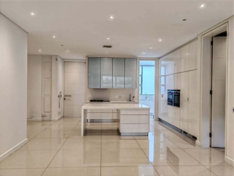 Modern, minimalist kitchen featuring high-gloss cabinetry, a central island, built-in oven, and polished tiled flooring with recessed ceiling lighting.