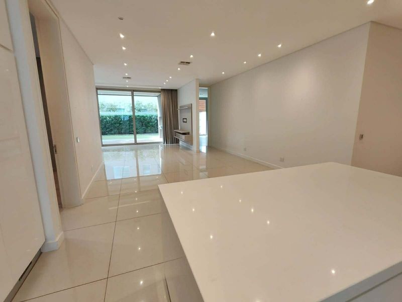 Spacious open-plan living area featuring polished porcelain tiles, recessed lighting, and a modern kitchen island, leading out to a private patio.