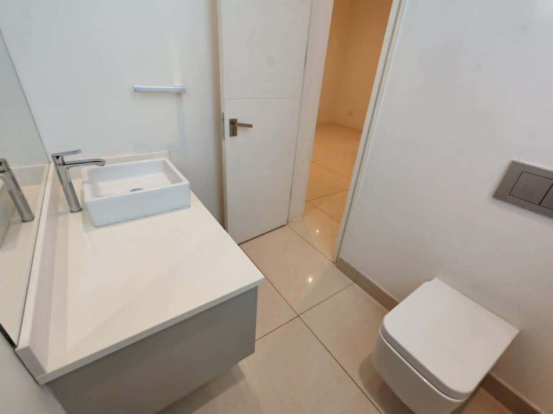 A modern, minimalist bathroom featuring a wall-mounted toilet, a sleek vanity with a vessel sink, and neutral tiled flooring.