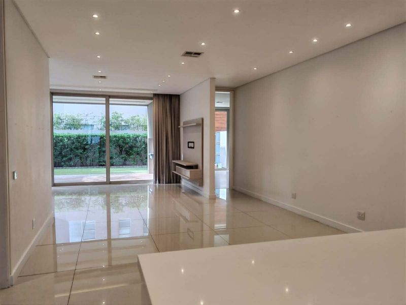 Spacious, modern living area featuring polished tile floors, recessed lighting, and large sliding glass doors opening to a private garden view.