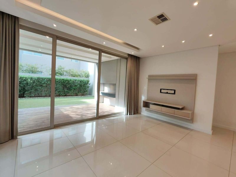 Spacious living room featuring large sliding glass doors opening to a patio, polished floor tiles, and a modern built-in media console.