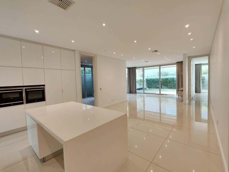 Spacious open-plan living and kitchen area featuring high-gloss cabinetry, a central island, large format floor tiles, and seamless access to the rear garden.