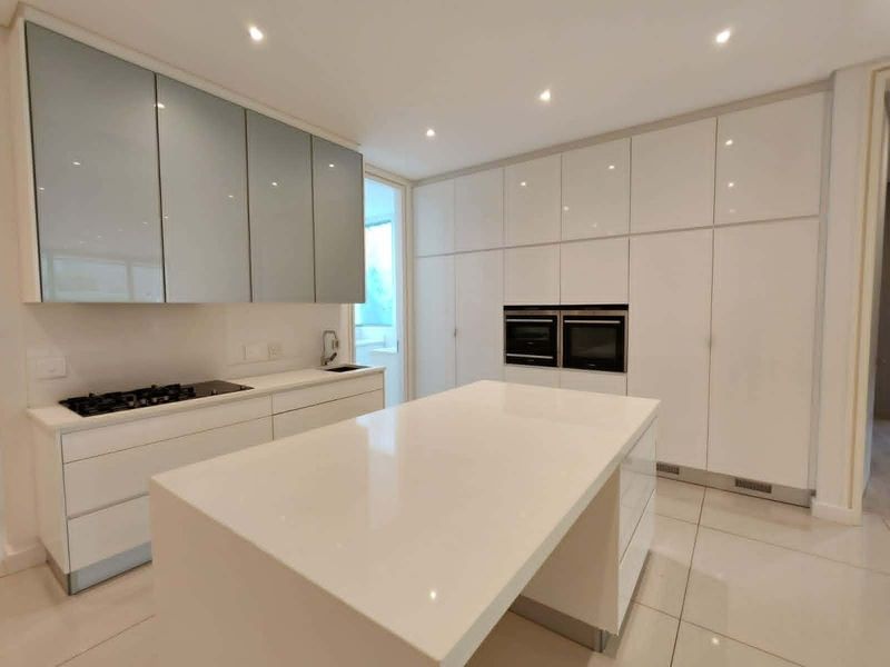 Modern kitchen featuring high-gloss cabinetry, a central island with stone countertops, integrated double ovens, and a gas hob with recessed lighting.