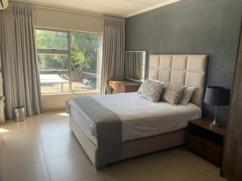 A well-maintained bedroom featuring large windows, neutral tiled flooring, and a dark textured accent wall.