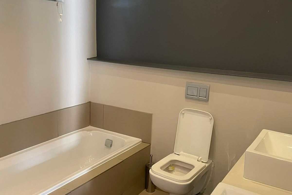 Modern bathroom featuring a built-in bathtub, wall-hung toilet, and dual vanity basins with neutral tiling and a dark accent wall.