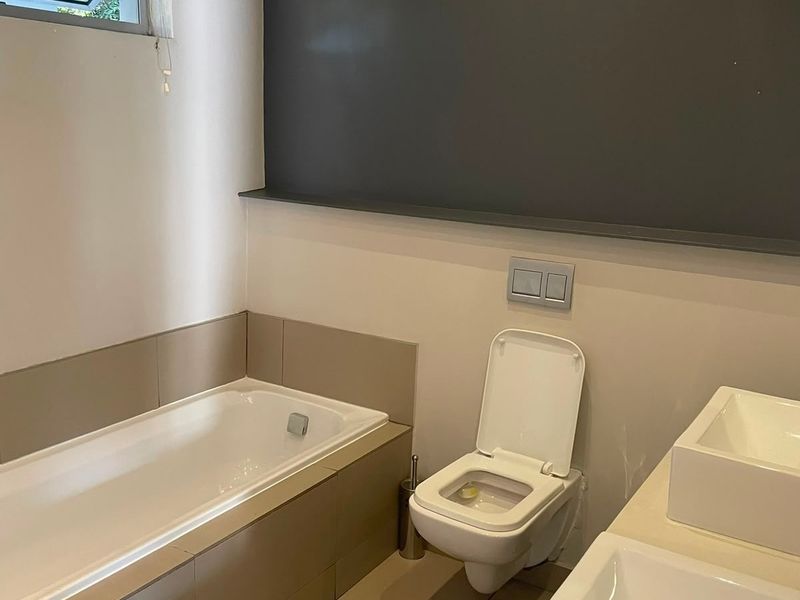Modern bathroom featuring a built-in bathtub, wall-hung toilet, and dual vanity basins with neutral tiling and a dark accent wall.