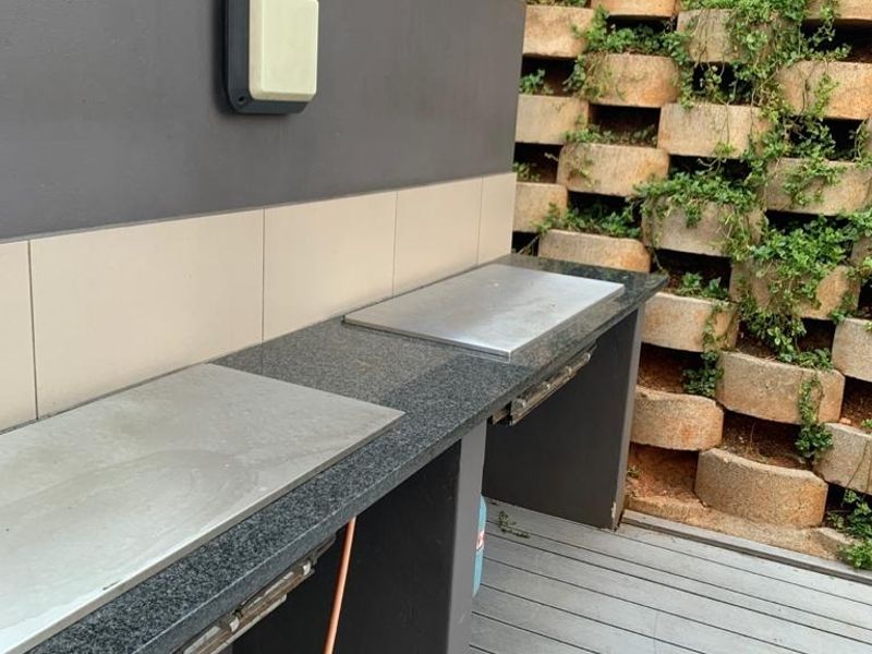 Outdoor patio area featuring a built-in granite countertop with an integrated gas grill, set against a landscaped retaining wall and timber decking.