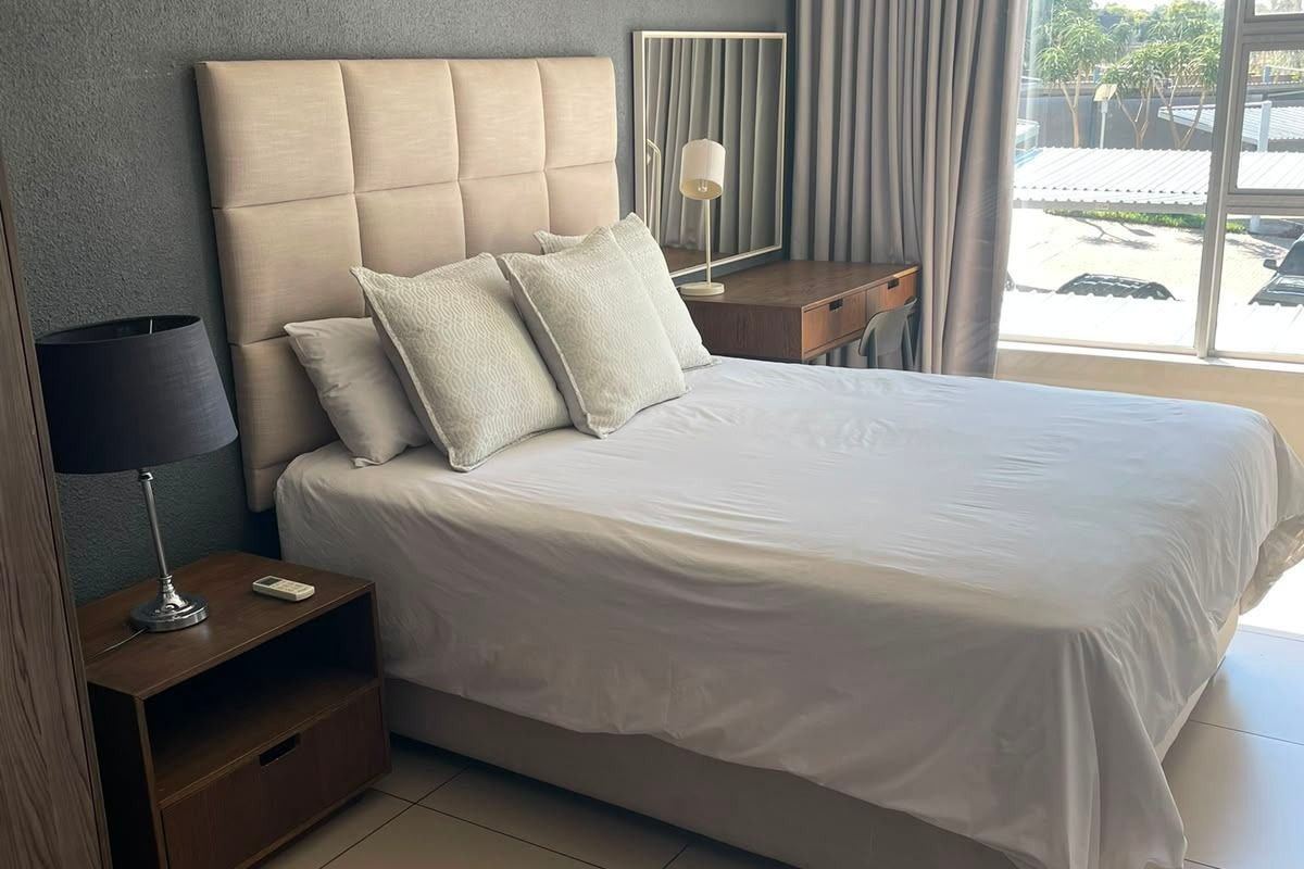 A well-maintained bedroom featuring large windows, neutral tiled flooring, and a feature wall, offering a bright and comfortable living space.