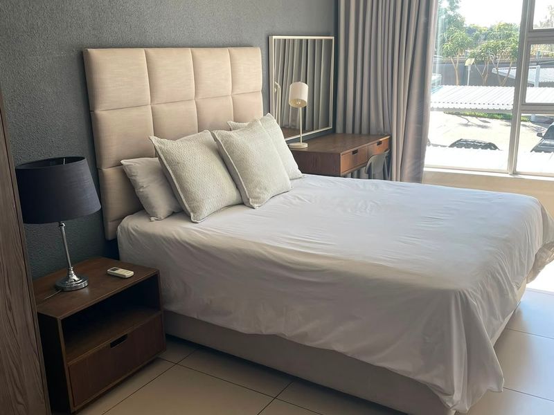 A well-maintained bedroom featuring large windows, neutral tiled flooring, and a feature wall, offering a bright and comfortable living space.