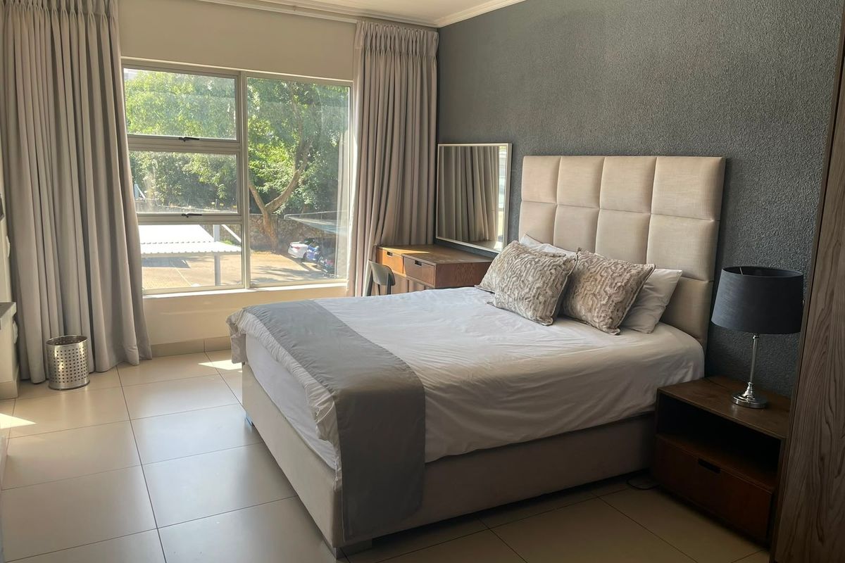 A well-maintained bedroom featuring large windows, neutral tiled flooring, and a dark textured accent wall.