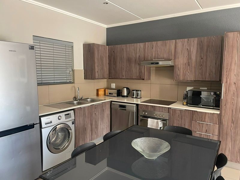 Modern open-plan kitchen featuring wood-grain cabinetry, integrated appliances, tiled backsplash, and functional layout with ample storage and workspace.