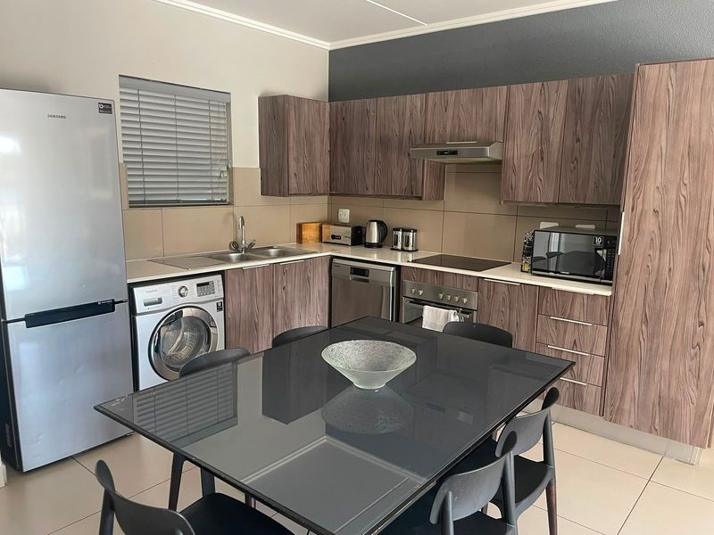 Modern open-plan kitchen featuring wood-grain cabinetry, integrated appliances, and tiled flooring, seamlessly flowing into the dining area.