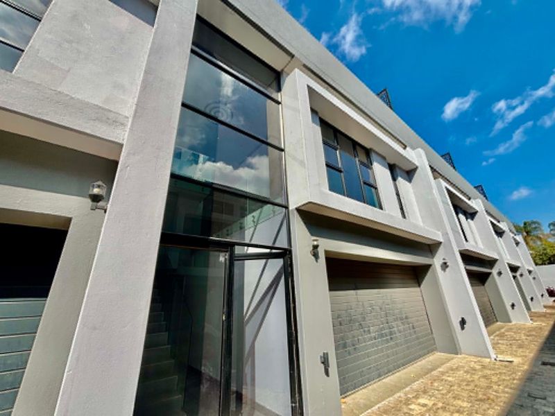 Modern townhouse exterior featuring a striking double-height glass entrance, contemporary grey facade, and integrated garage access.