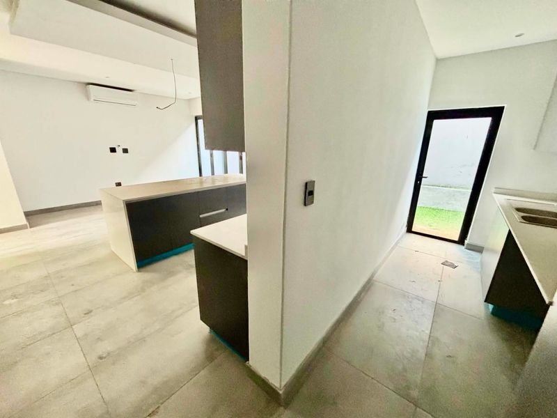 Modern open-plan kitchen and living area featuring sleek cabinetry, stone countertops, tiled floors, and direct access to the outdoor space.