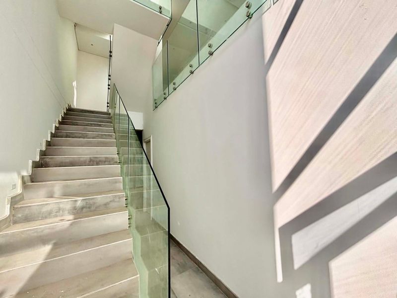 Modern hallway featuring a concrete staircase with a sleek glass balustrade, clean white walls, and neutral tiled flooring.