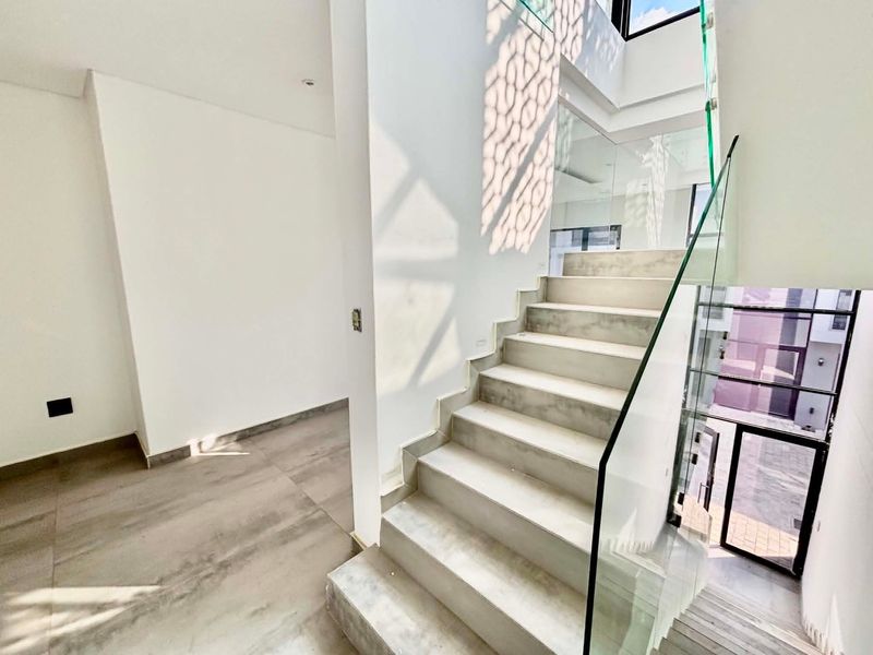 Modern interior hallway featuring a sleek staircase with glass balustrades and large format floor tiles, creating a bright and contemporary architectural space.