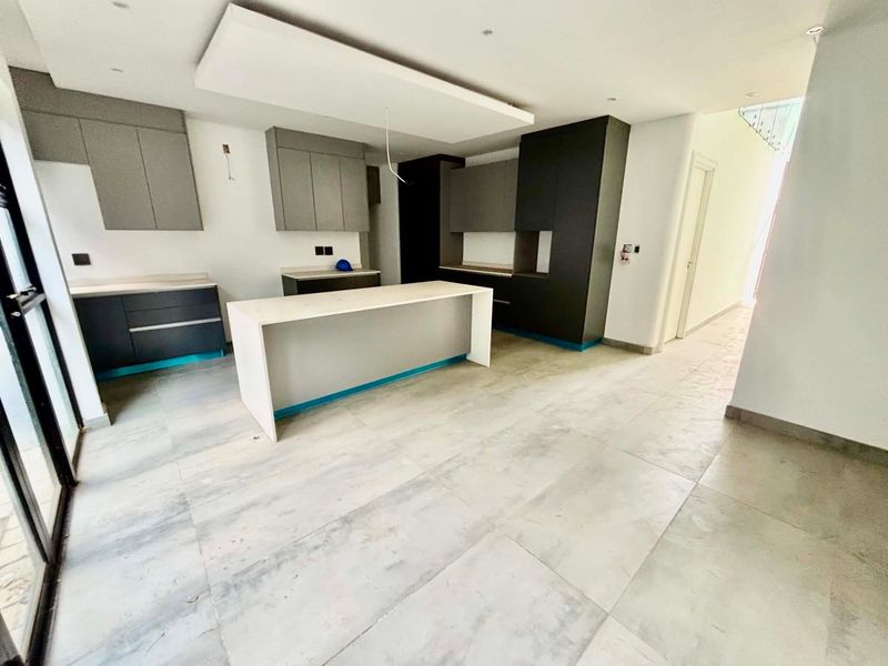 Modern, unfinished kitchen featuring sleek grey cabinetry, a central island with stone countertops, and large format floor tiles in an open-plan layout.