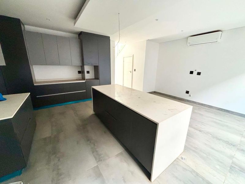Modern open-plan kitchen featuring dark cabinetry, a central stone island, and tiled flooring, ready for final finishing touches.