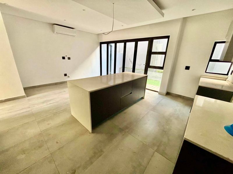 Modern open-plan kitchen and living area featuring a central island, stone countertops, tiled flooring, and large sliding doors leading to the outdoor space.