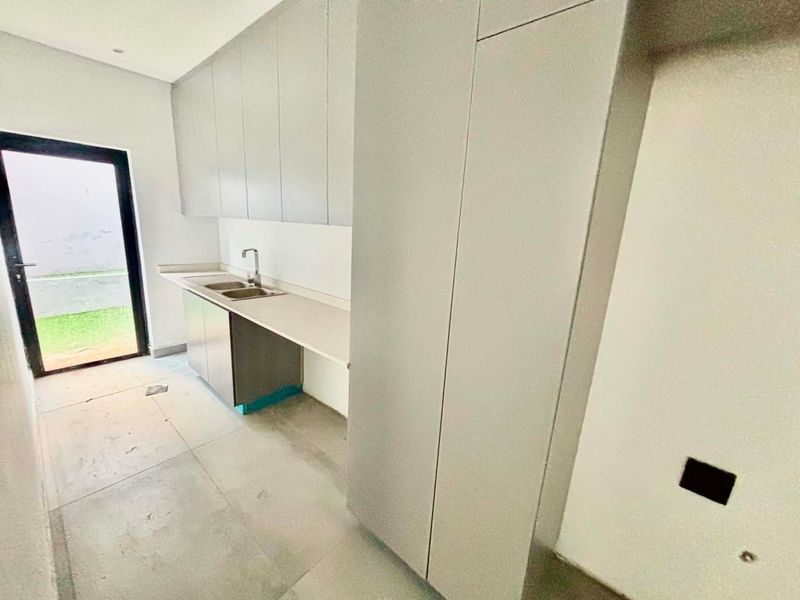 A modern, empty kitchen featuring sleek grey cabinetry, a double sink, and direct access to the outdoor area through a glass door.