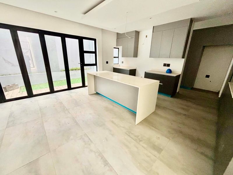 Modern open-plan kitchen area featuring a central island, sleek cabinetry, and large glass sliding doors leading to the outdoor space.