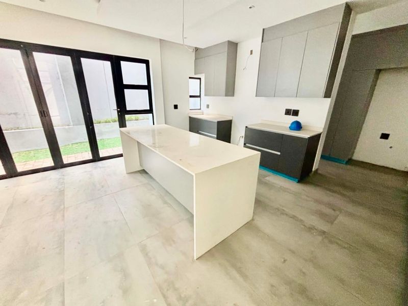 Modern, newly installed kitchen featuring a central island, stone countertops, and sleek cabinetry, opening directly to an outdoor patio area.