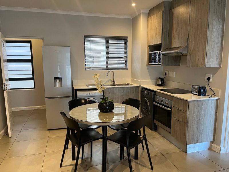 Modern open-plan kitchen featuring wood-look cabinetry, integrated appliances, tiled flooring, and a functional layout with adjacent dining space.