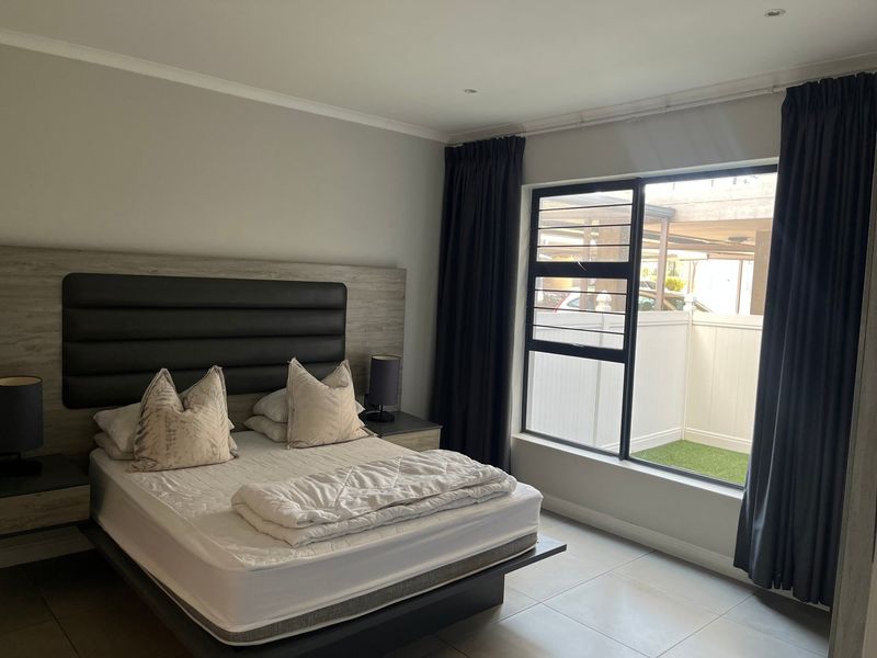 A well-maintained bedroom featuring tiled flooring, recessed downlighting, and a large sliding window with views of the outdoor area.