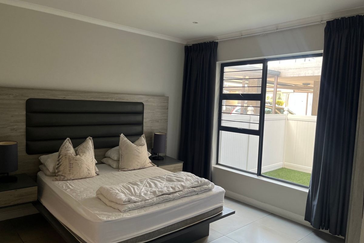 A well-maintained bedroom featuring tiled flooring, recessed downlighting, and a large sliding window with views of the outdoor area.