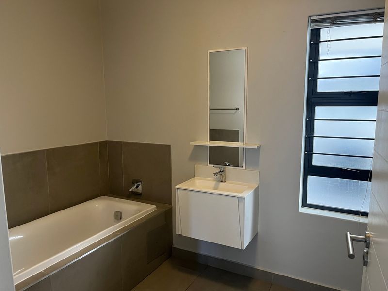 A clean, modern bathroom featuring a built-in bathtub, wall-mounted vanity with basin, and a louver window for natural ventilation.