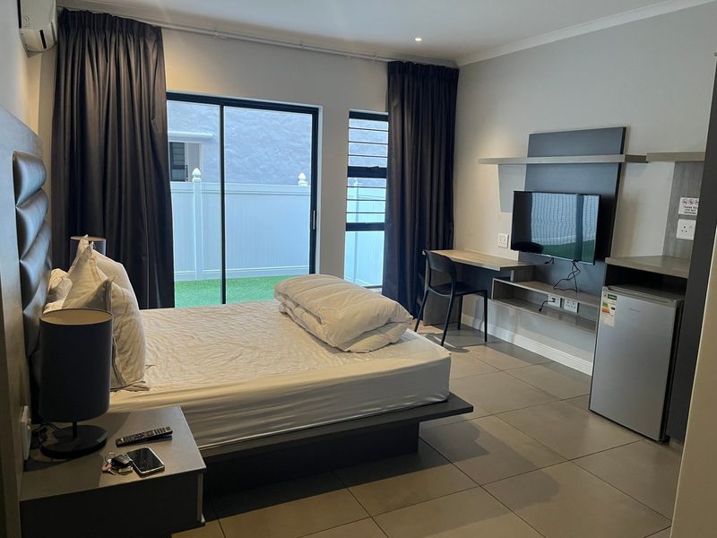 Modern bedroom featuring tiled floors, a wall-mounted desk and shelving unit, air conditioning, and sliding glass doors providing access to an outdoor area.