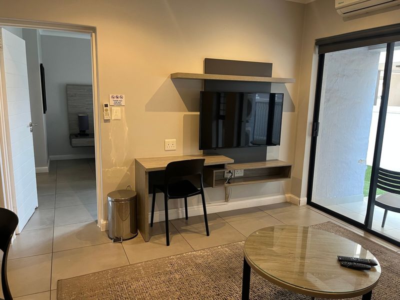 A modern living area featuring a wall-mounted media console, integrated desk space, tiled flooring, and direct access to an outdoor patio through sliding glass doors.
