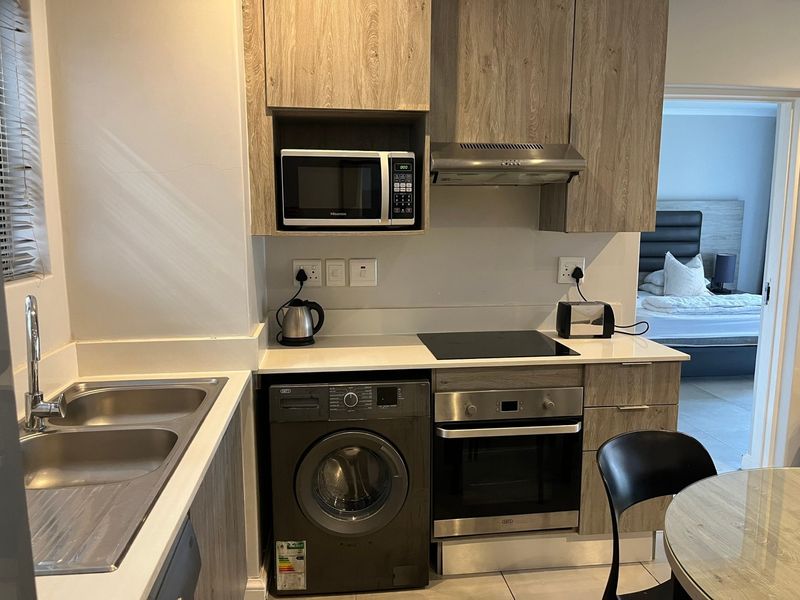 Modern kitchen featuring wood-look cabinetry, stone countertops, integrated oven, hob, extractor fan, and built-in microwave, with a double sink and laundry appliance space.
