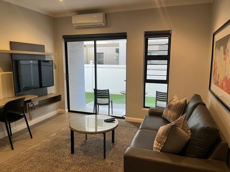 A well-maintained living room featuring tiled floors, a built-in media console, split-system air conditioning, and direct access to a private patio area.