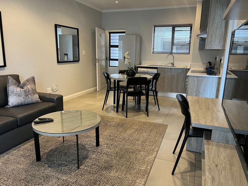 Open-plan living and kitchen area featuring modern wood-look cabinetry, tiled flooring, and a functional breakfast bar layout.