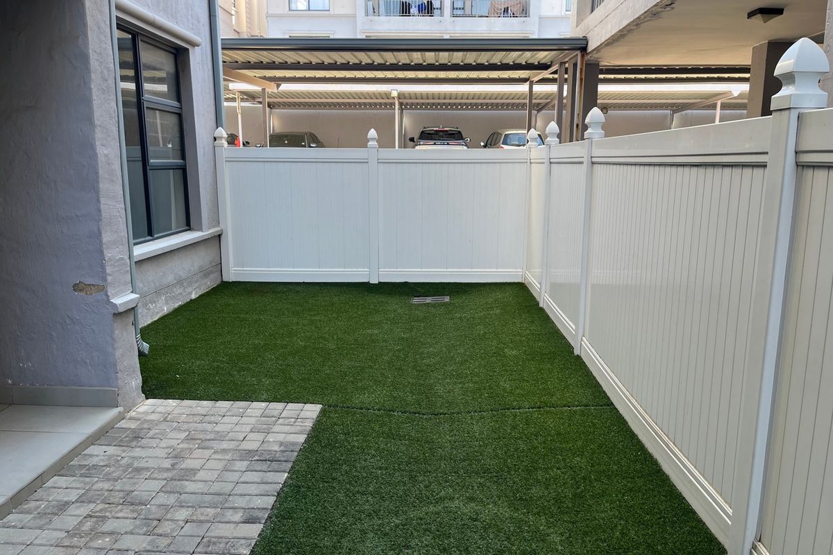 A private rear courtyard featuring artificial turf, paved section, and white vinyl privacy fencing.
