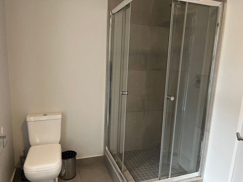 A clean, functional bathroom featuring a glass-enclosed shower and a standard toilet with neutral wall and floor tiling.
