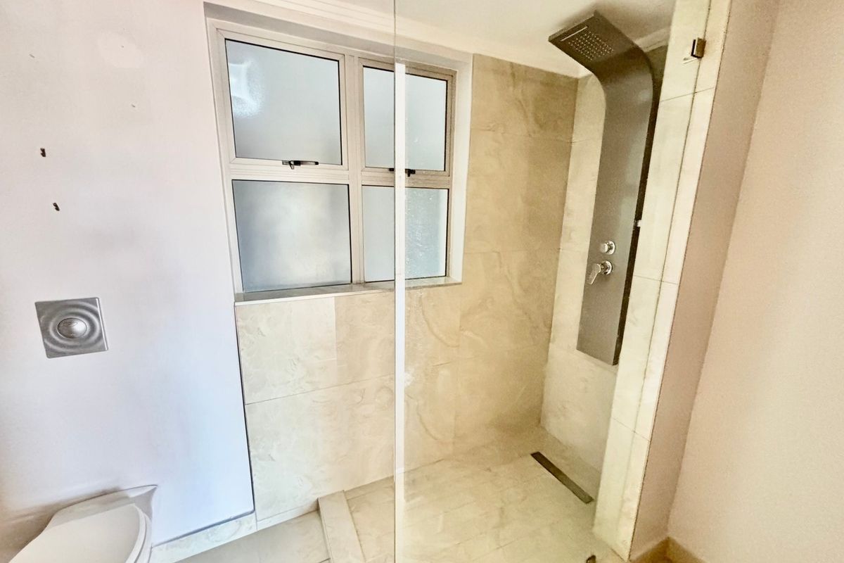 A modern bathroom featuring a walk-in shower with a sleek shower panel, glass screen, and neutral tiled finishes throughout.