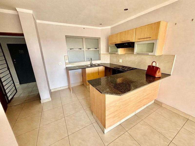 A functional kitchen featuring granite countertops, light wood cabinetry, an electric hob with extractor fan, and tiled flooring.