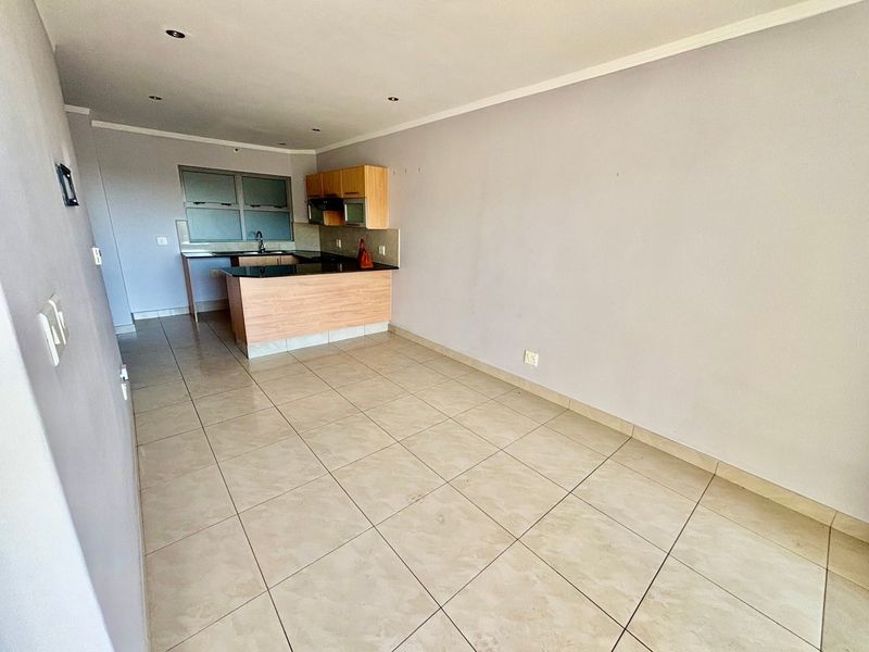 An open-plan living and kitchen area featuring neutral tiled flooring, recessed lighting, and built-in kitchen cabinetry with a breakfast counter.