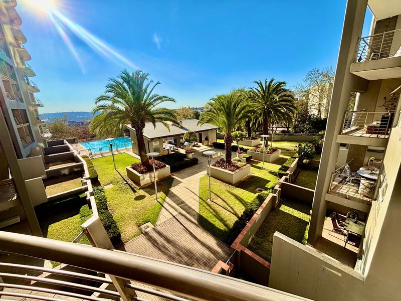 Elevated view of a well-maintained apartment complex courtyard featuring a swimming pool, landscaped gardens, and paved walkways.
