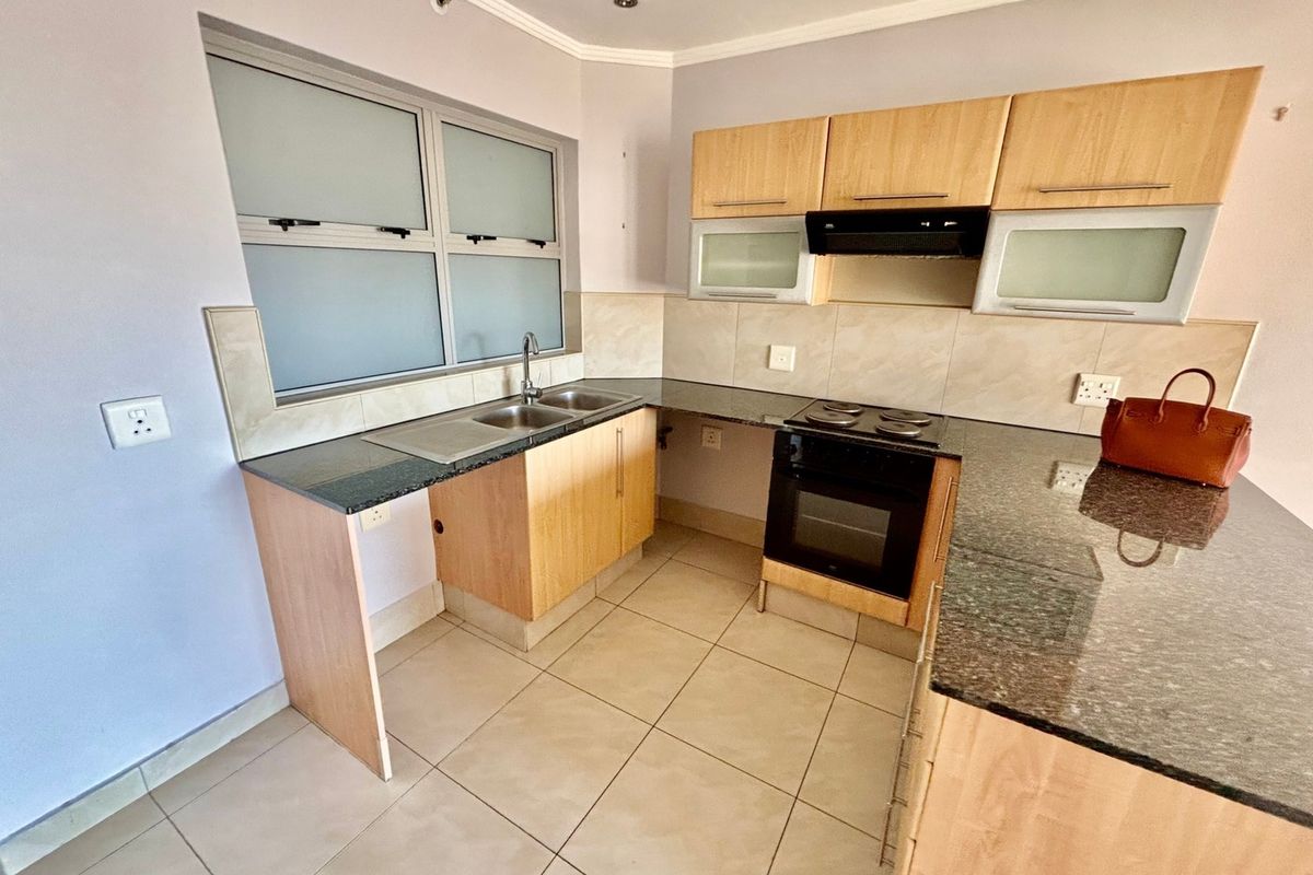 A functional kitchen featuring granite countertops, built-in oven with extractor fan, double sink, and tiled flooring with ample cabinetry.
