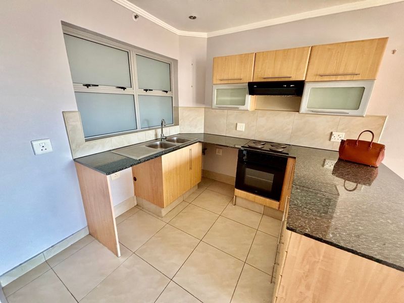 A functional kitchen featuring granite countertops, built-in oven with extractor fan, double sink, and tiled flooring with ample cabinetry.