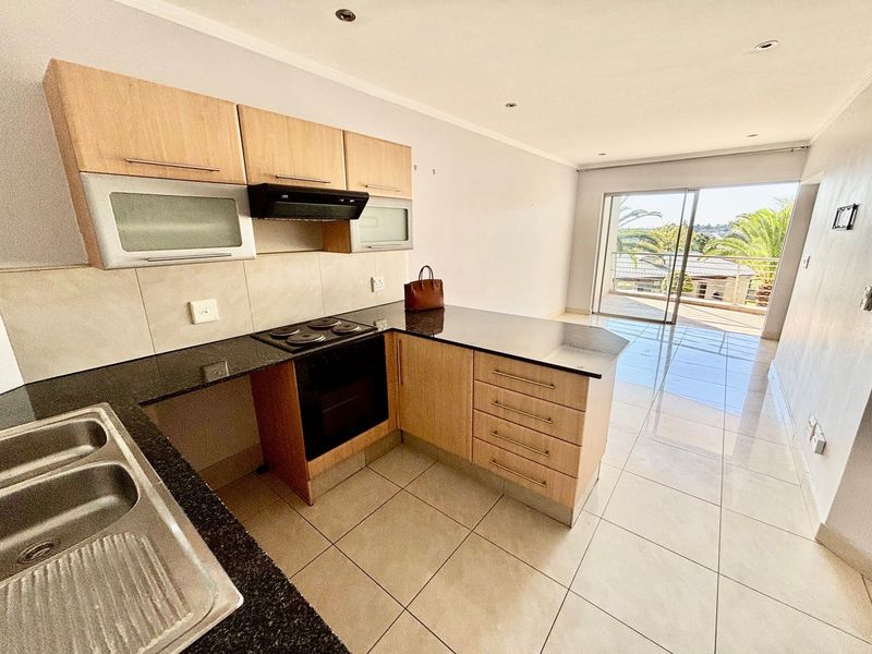 Open-plan kitchen and living area featuring modern cabinetry, granite countertops, tiled flooring, and direct access to a balcony through sliding glass doors.