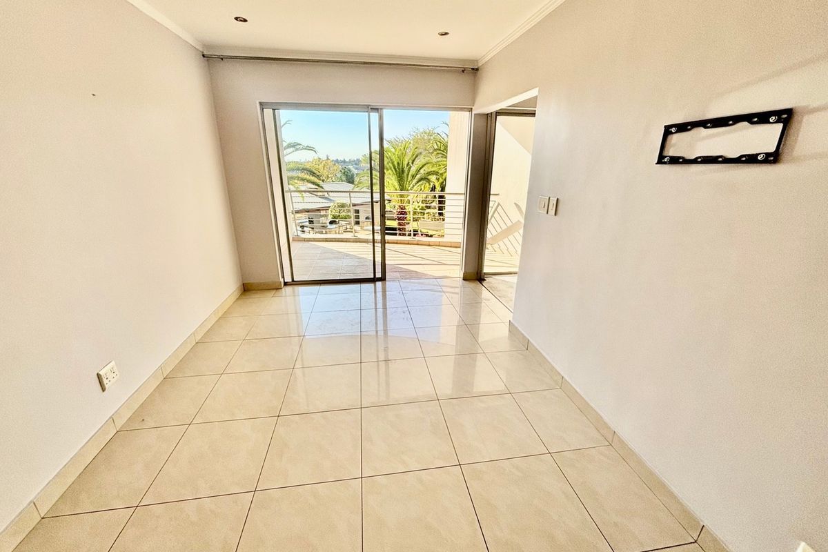 An empty, bright living room featuring neutral tiled flooring, recessed lighting, and a sliding glass door leading to an outdoor balcony area.