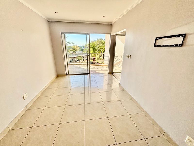 An empty, bright living room featuring neutral tiled flooring, recessed lighting, and a sliding glass door leading to an outdoor balcony area.